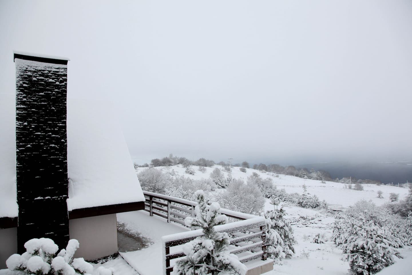 A snow-covered landscape with a modern building featuring a black facade and a sloped roof.