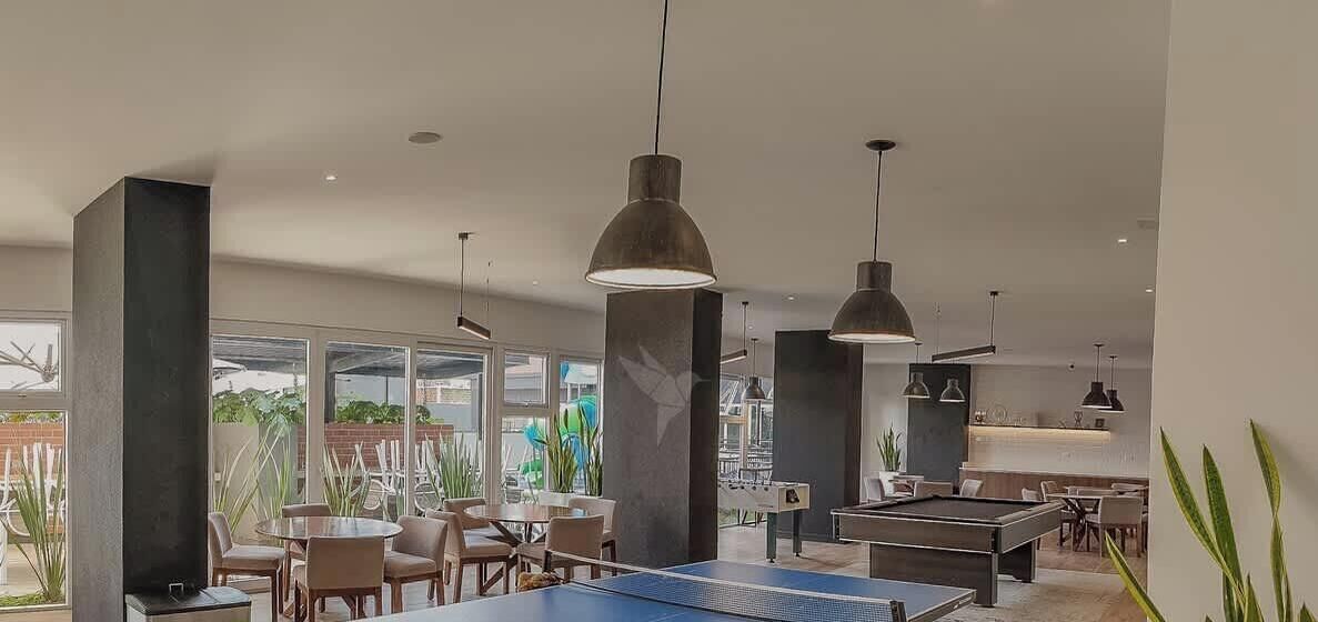 Un espacio interior moderno con mesa de ping pong, zona de estar y ventanas amplias que ofrecen vistas al exterior.