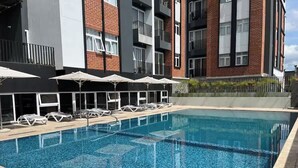 A swimming pool with lounge chairs and umbrellas, surrounded by a modern building with brick and glass elements. - Luxury Skyline City View KING Bed FREE Pool & Gym (Ciudad de Guatemala)