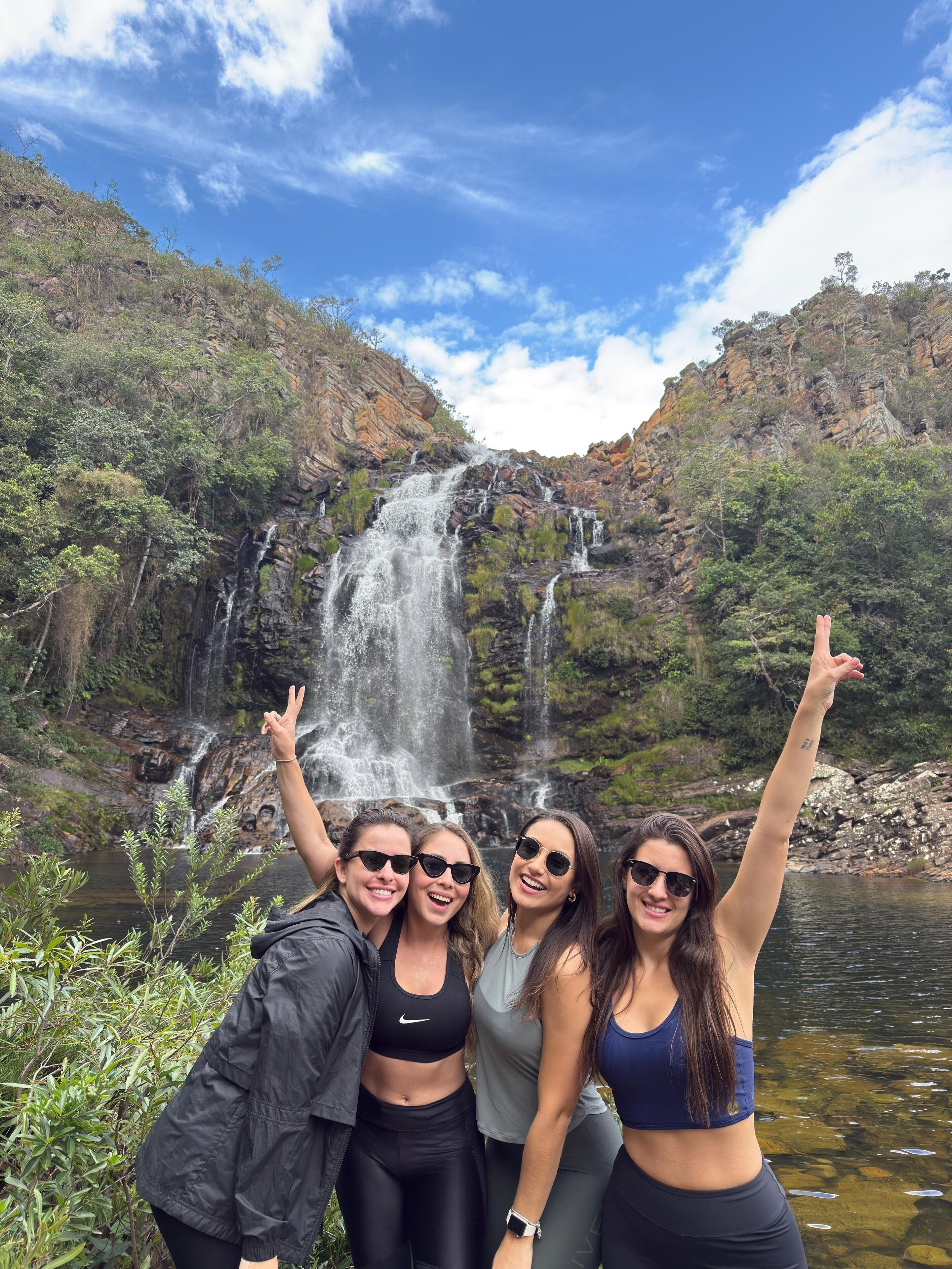 A group of people posing in front of a waterfall with a rocky landscape and greenery in the background.