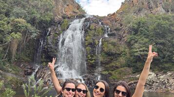 A group of people posing in front of a waterfall with a rocky landscape and greenery in the background.