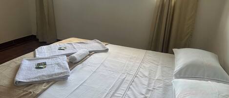 Habitación de hotel con cama, ropa de cama blanca, ventana con cortinas y vistas al exterior.