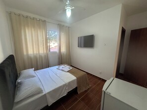 A hotel room with a bed, a TV, a ceiling fan, and a window with curtains. - Pousada Rio Cipó (Santana do Riacho)