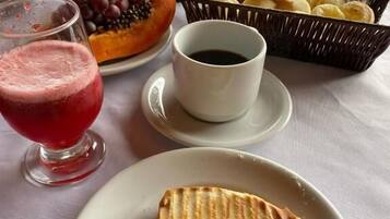 Une table mise pour le petit-déjeuner avec un sandwich, un saladier de fruits, une tasse de café et un verre de jus de fruits.