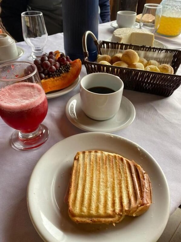 A breakfast setting with a sandwich, a fruit bowl, a cup of coffee, and a glass of juice.