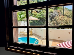 Ein Fenster mit Blick auf einen Pool, Stühle und ein rot gestreiftes Kissen.