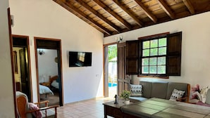 Una sala de estar con techo de madera, televisor montado en la pared, sofá, mesa de centro y ventana con vista a la vegetación.