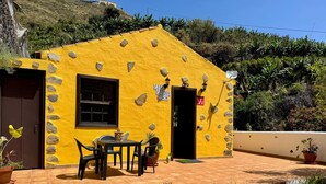 Un edificio amarillo con puerta, ventana y zona de estar exterior con macetas.