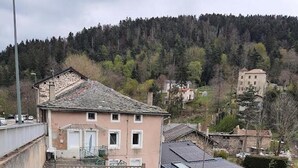 A two-story house with a stone facade and a tiled roof, surrounded by a grassy area and a forested hill in the background. - Little corner of Paradise (Yssingeaux)