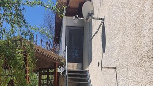 A wooden staircase leading to a door, a satellite dish on the building, and a pergola with climbing plants. - Little corner of Paradise (Yssingeaux)