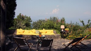 A patio with two lounge chairs, a yellow cushioned sofa, a table with a lamp, and a view of the sea. - Villa Rosa in Marina di Maratea (Marina)