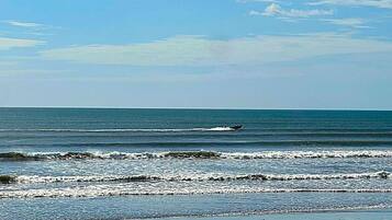 A beach with waves, a boat, and a clear sky.
