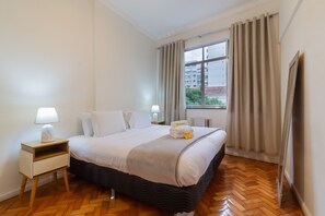 Una camera d'albergo con un letto, un comodino, una lampada e una finestra con tende.