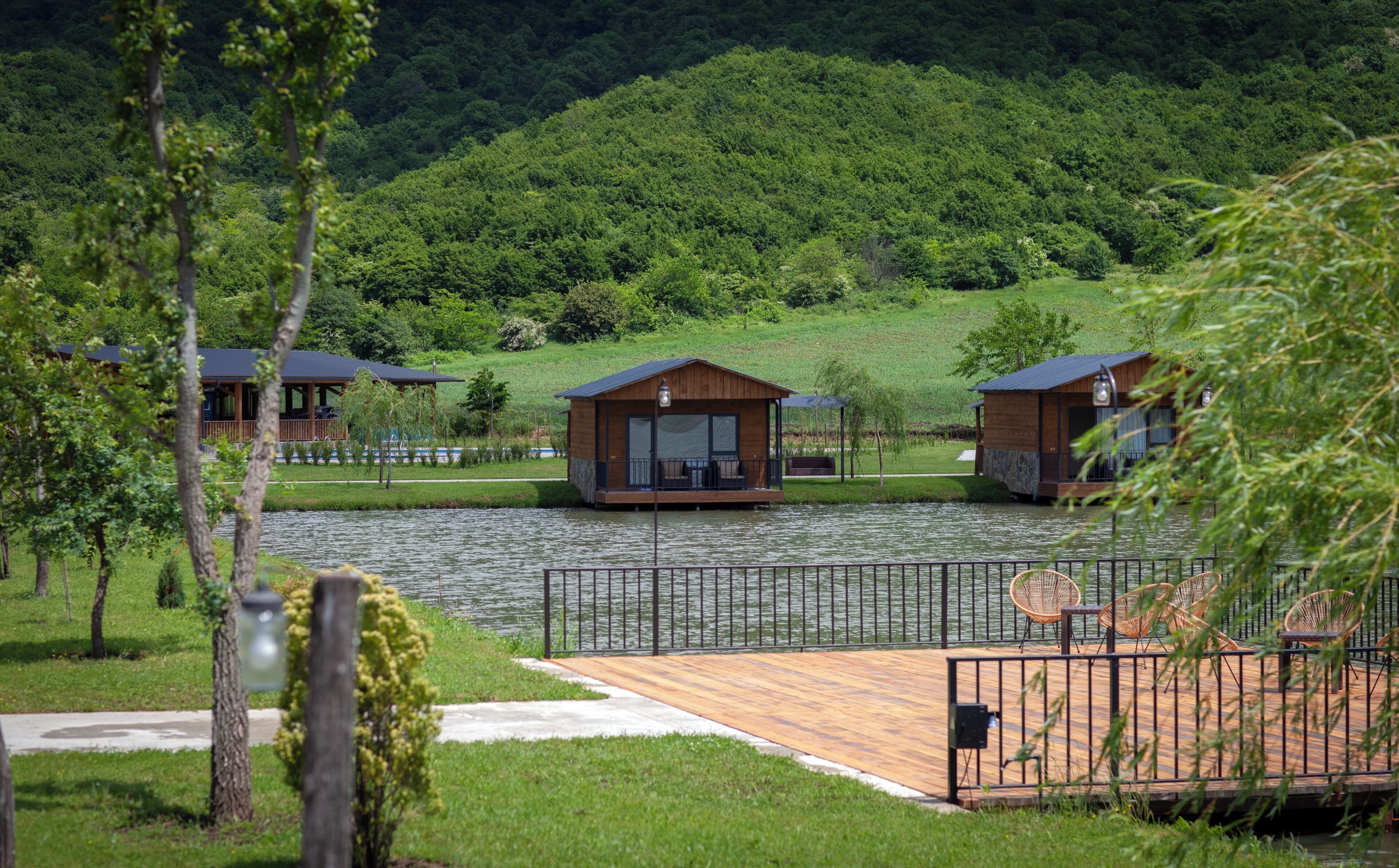 A lakeside resort with wooden cabins, a wooden deck, and a metal fence.