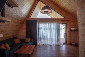 Een houten interieur met een schuine balkenkap, een bank, een tafel en uitzicht door een raam.