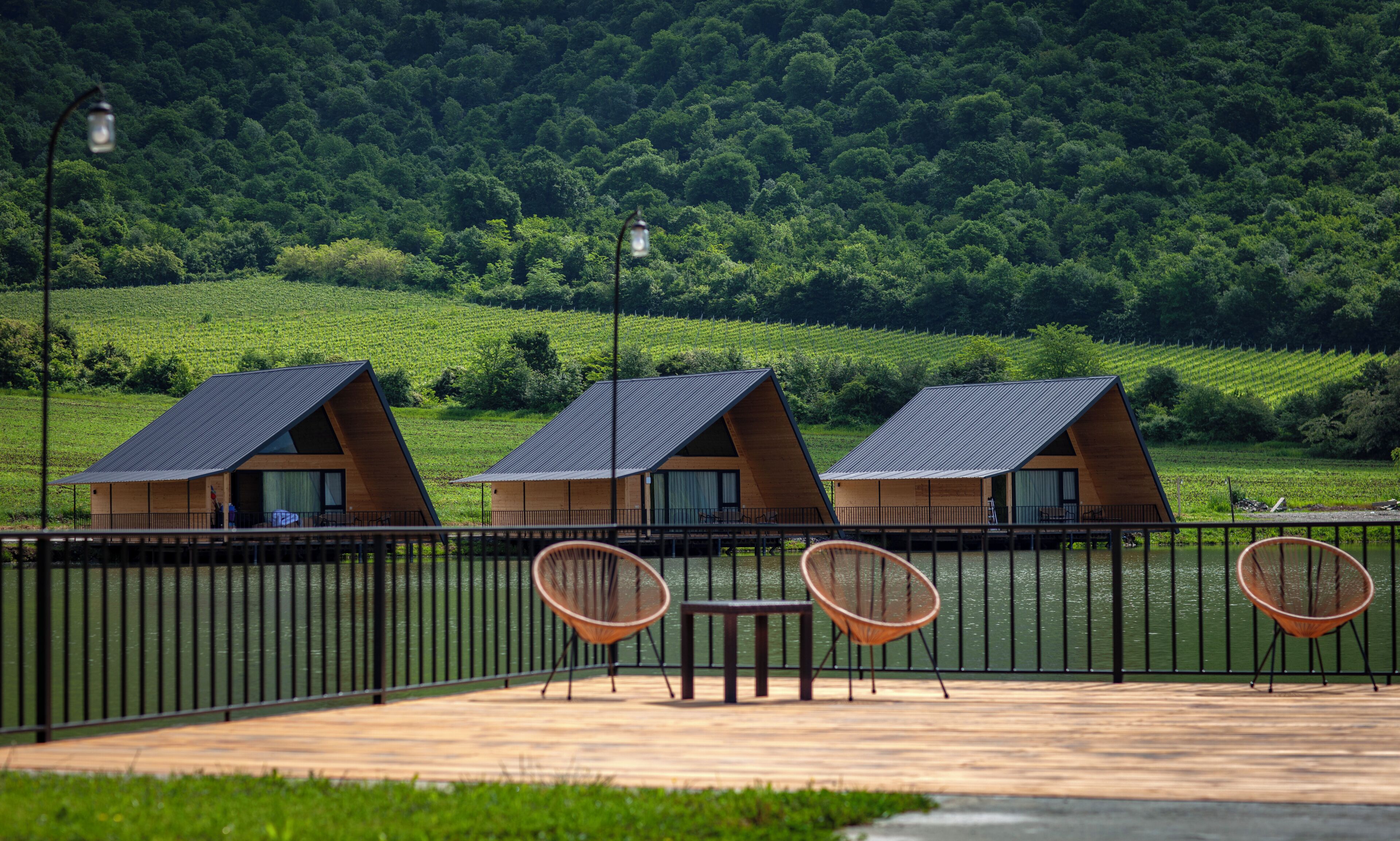Three wooden cabins with sloped roofs, a wooden deck, and a metal railing.