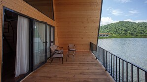 Eine Holzterrasse mit Blick auf einen See und Hügel, zwei Stühle und eine Glastür.