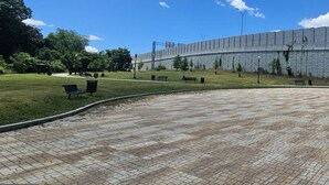 Un chemin pavé bordé de bancs, une pelouse et un bâtiment à la façade en pierre.
