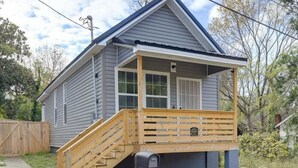 Une maison de plain-pied avec un porche à l’avant, un escalier en bois et une boîte aux lettres.
