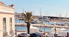 Uma marina com barcos, uma palmeira e carros estacionados.