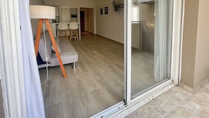 Un apartamento moderno con un ventanal corredero que da a un balcón, un sofá, un comedor y una cocina.