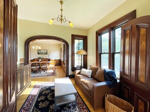 A spacious living room with a brown leather sofa, a dining area with a wooden table and chairs, and a chandelier.