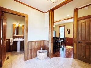 A hallway with wooden walls, a sink, a mirror, a basket, and a dining area with chairs.