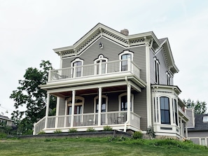 Une maison à deux étages avec un balcon, une véranda qui fait le tour de la maison et une cheminée.