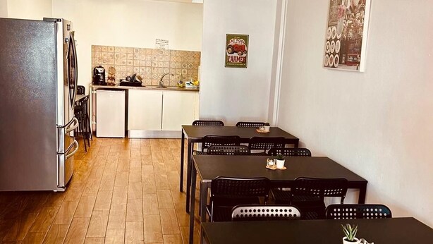 A dining area with tables and chairs, a kitchen in the background, and a hanging light fixture. - Lagos Marina- 7nightdiscount- Twin Room (Lagos)