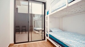 A room with a sliding glass door leading to a balcony, a bunk bed with patterned bedding, and a small table with chairs. - Lagos Marina- 7nightdiscount- Twin Room (Lagos)