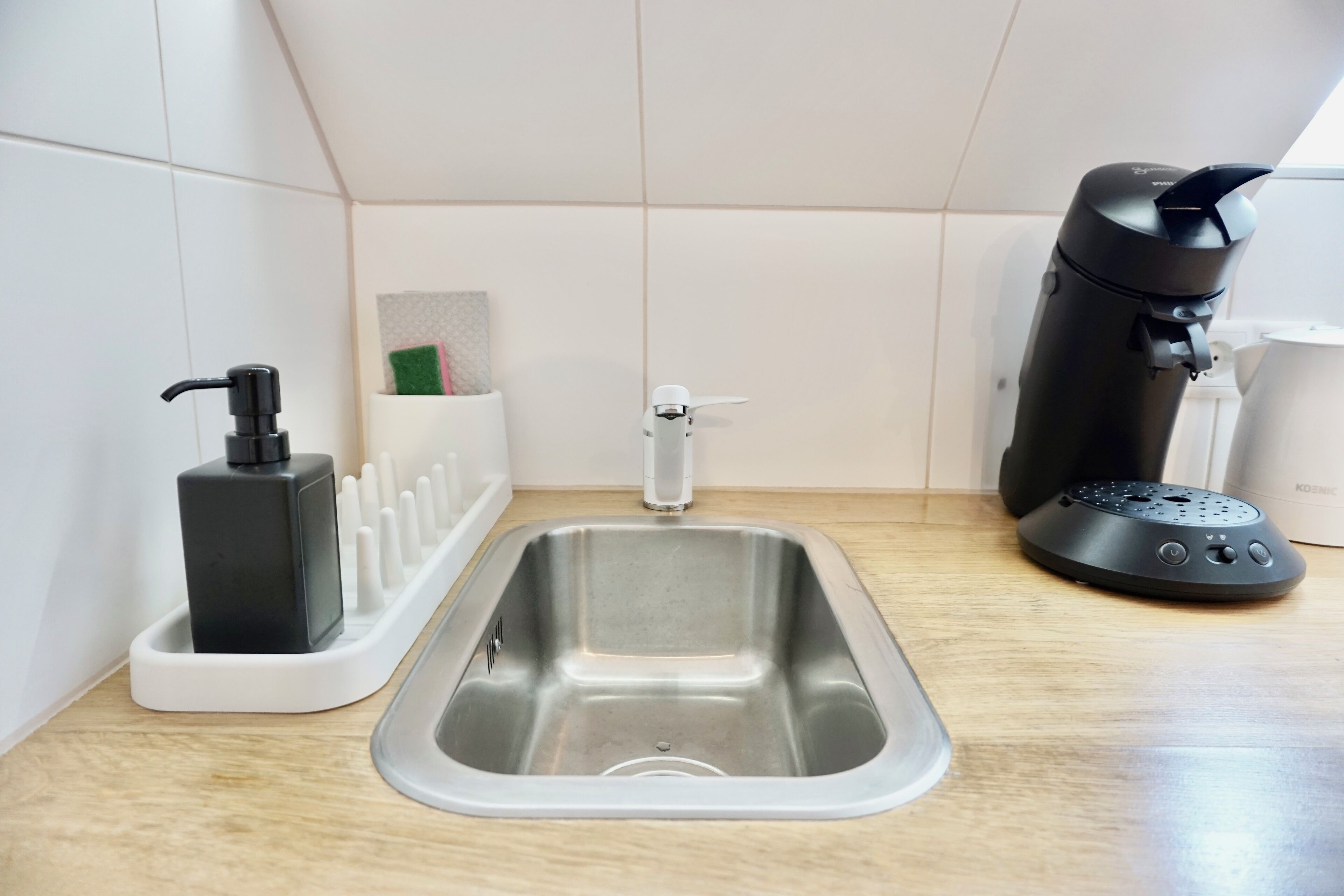 Una cocina moderna con un lavamanos de acero inoxidable, una cafetera y un dispensador de jabón.