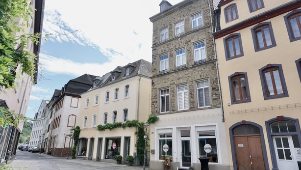 A street with historic buildings, including a café with outdoor seating and a shop with a visible sign. - Modern apt | old building I near the Rhine| view of the fortress | SmartTV (Koblenz)