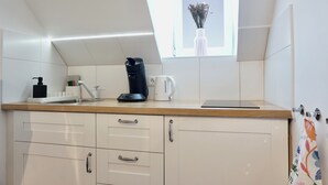 A kitchen with white cabinets, a wooden countertop, a coffee maker, a kettle, and a window with a vase of flowers. - Modern apt | old building I near the Rhine| view of the fortress | SmartTV (Koblenz)