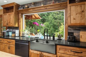 Cocina con armarios de madera, encimera negra, pileta de acero inoxidable y ventana con vista a follaje.