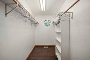 Un dressing accessible sans porte, doté d’un plancher en bois, de murs blancs et d’une fenêtre circulaire.