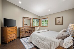 A bedroom with a bed, dresser, television, and windows.