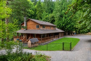 Une cabane en rondins à deux étages, dotée d’un porche, entourée d’une pelouse bien entretenue et d’une forêt dense.