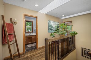 A hallway with a wooden railing, a wooden ladder, a red towel, a sink, and a framed picture on the wall.
