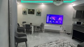 Een moderne woonkamer met een flatscreen televisie, een kroonluchter en een eethoek.