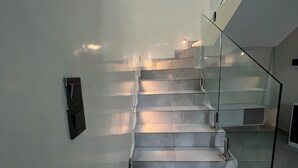 Een moderne trap met glazen leuning en een bedieningspaneel aan de muur.