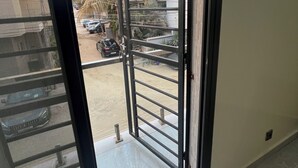 Een open metalen poort die leidt naar een parkeerplaats met auto’s en palmbomen.