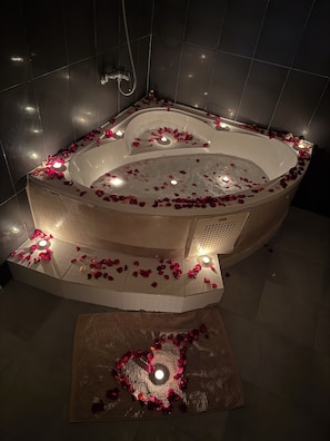 A modern bathroom with a freestanding bathtub surrounded by rose petals and candles, creating a romantic ambiance. - Serenity Mogador (Essaouira)