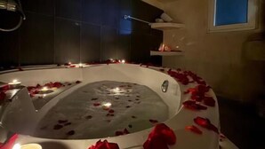 A hot tub surrounded by rose petals and candles, with a small shelf above it holding decorative items.