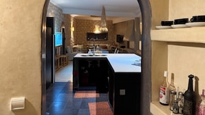 A modern kitchen with a central island, a stone accent wall, and a view into a living area through an archway.