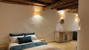 A bedroom with a wooden ceiling, a bed with a white and blue bedspread, two wall-mounted lights, and a decorative cabinet.