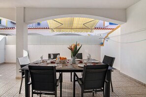 An outdoor dining area with a table set for four, chairs, a yellow umbrella, and a potted plant.