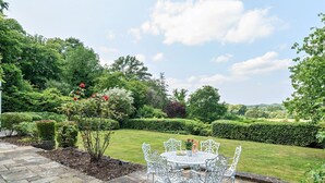 A garden patio with a round table and chairs, surrounded by well-maintained hedges and flowering plants. - 5bed Surrey home · Games Room · Near Thorpe Park - Pass the Keys (Surrey)