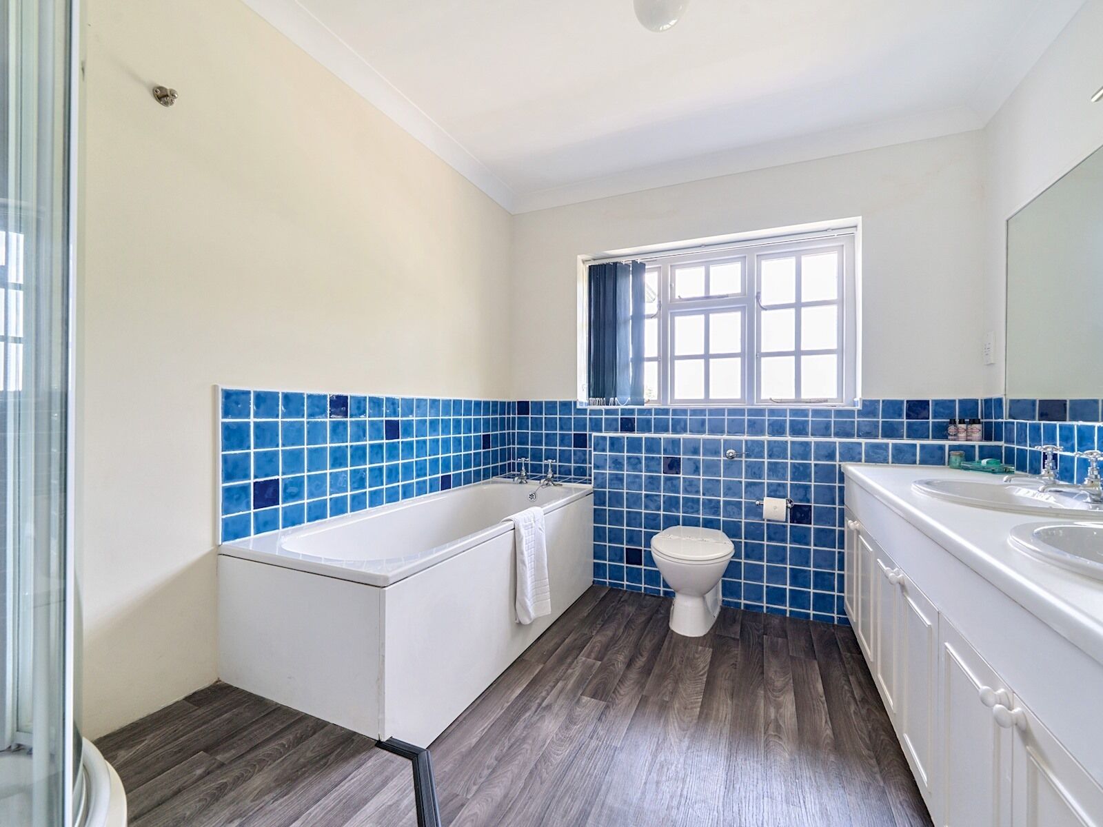 A bathroom with a bathtub, toilet, and sink, featuring blue-tiled walls and wooden flooring.