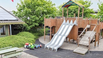 Ein Spielplatz mit Rutsche, Kletterbereich und einem Picknicktisch mit Spielzeugautos.