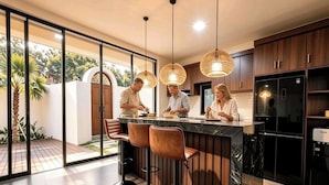 Une cuisine moderne dotée d’un îlot central, de tabourets de bar, de luminaires suspendus et offrant une vue sur l’extérieur.